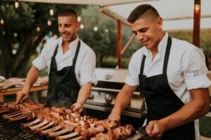 Dois jovens a fazer churrasco ao ar livre.